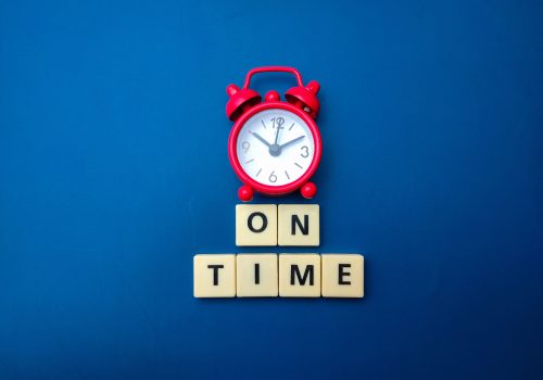 Red alarm clock with the word ON TIME isolated on a blue background.